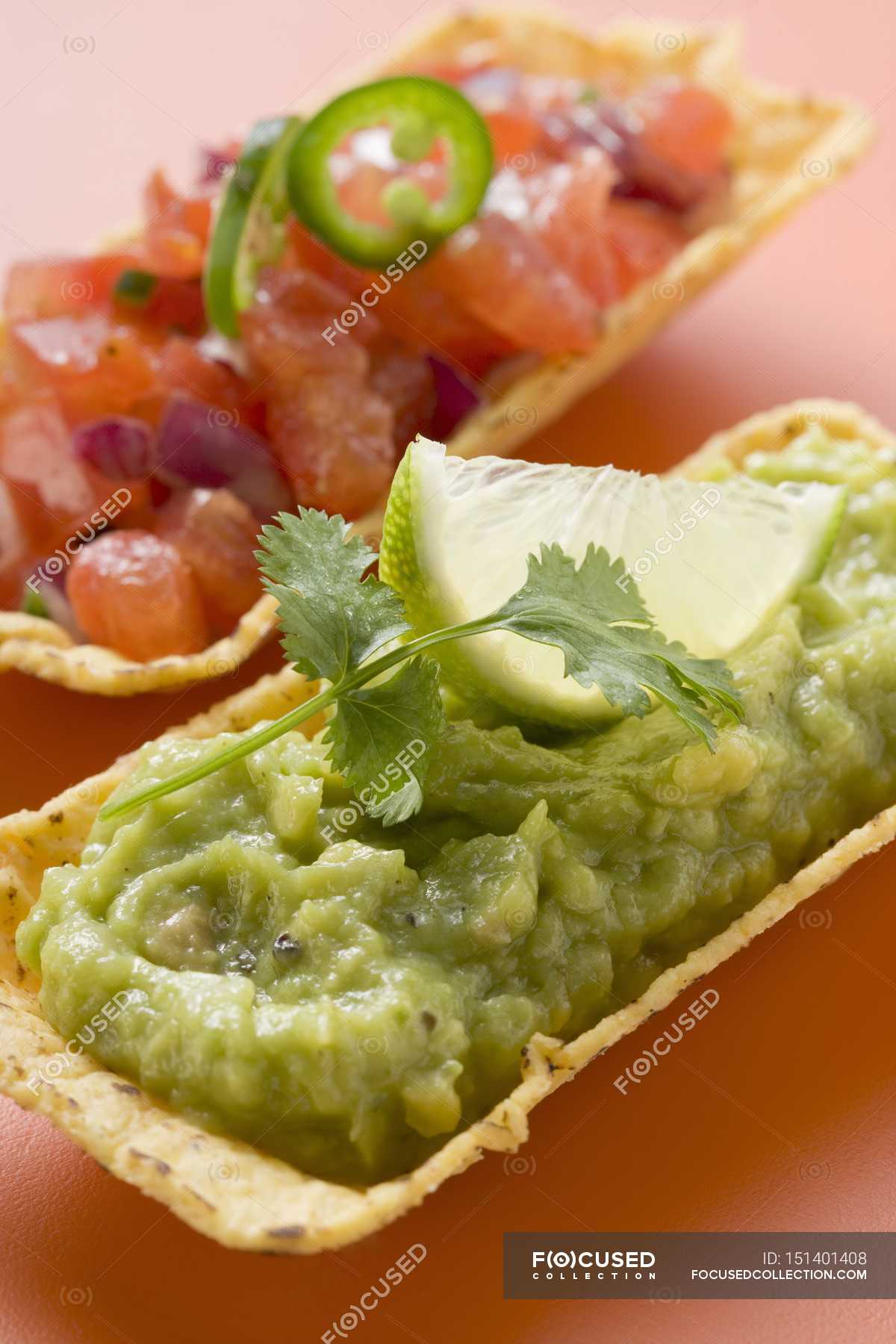 Guacamole y salsa de tomate en conchas de taco sobre superficie rosa ...