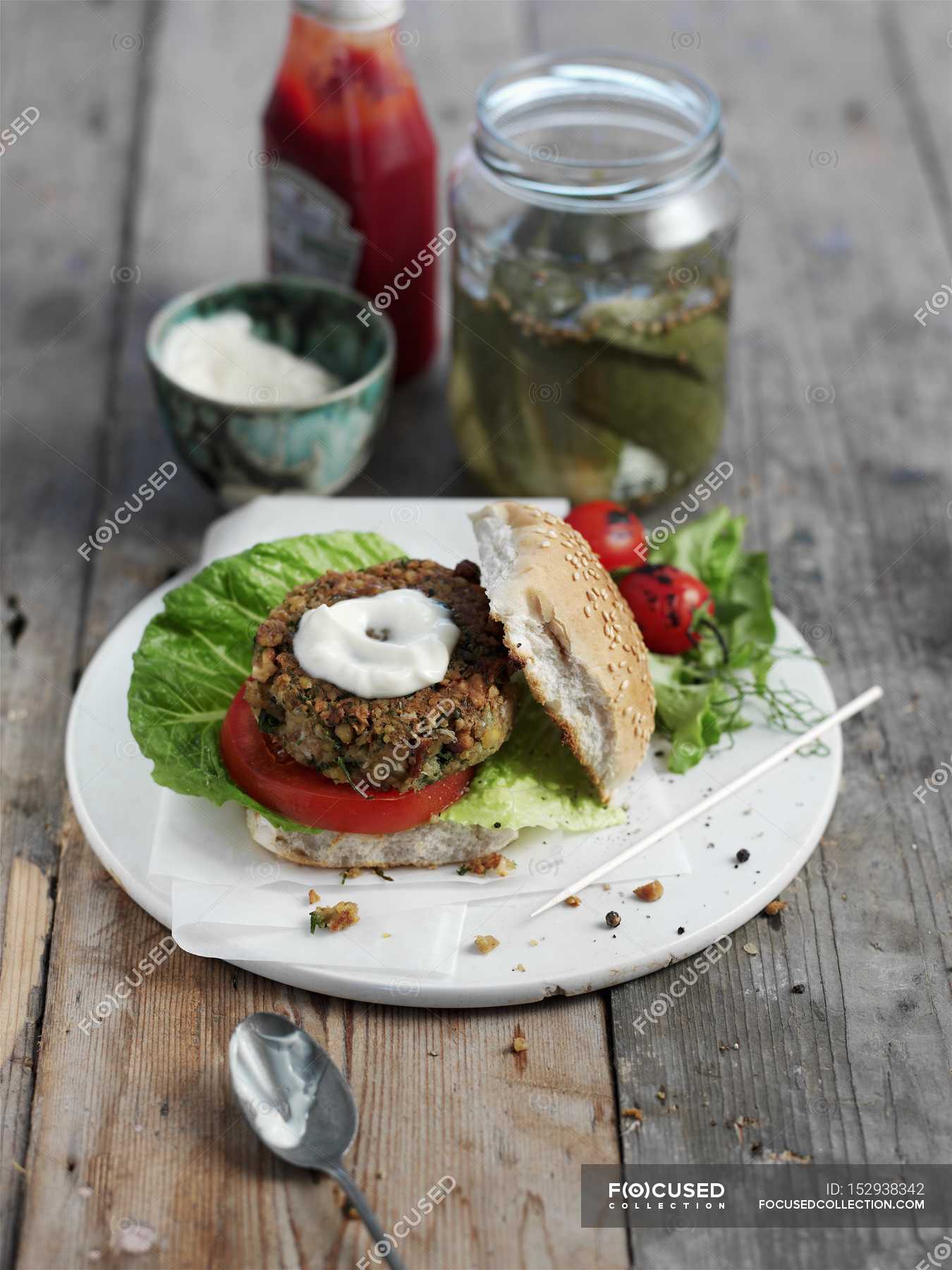 A chickpea burger with yogurt and gherkins on white plate over wooden