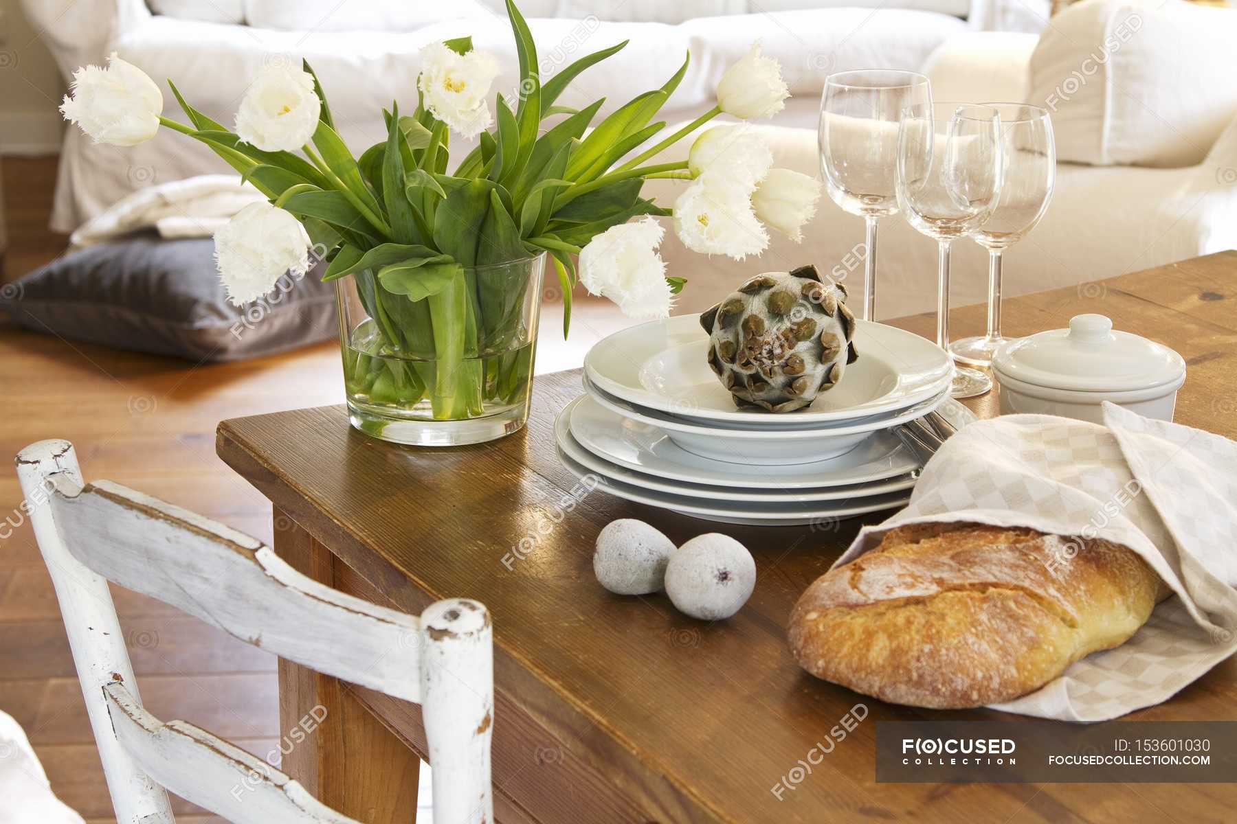 A Bunch Of White Tulips In A Glass Vase Next To A Stack Of Plates
