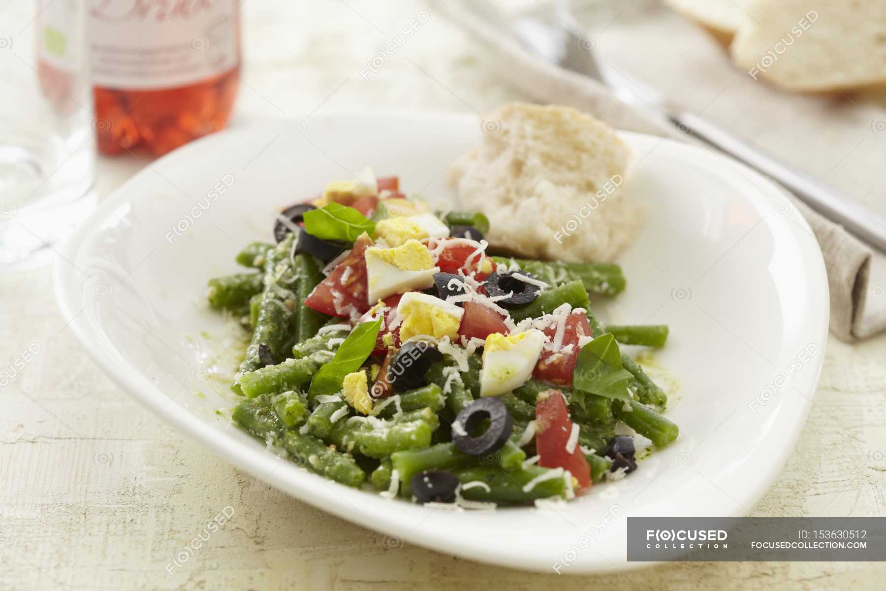 Bean salad with olives, tomatoes and egg on white plate — meal, cuisine