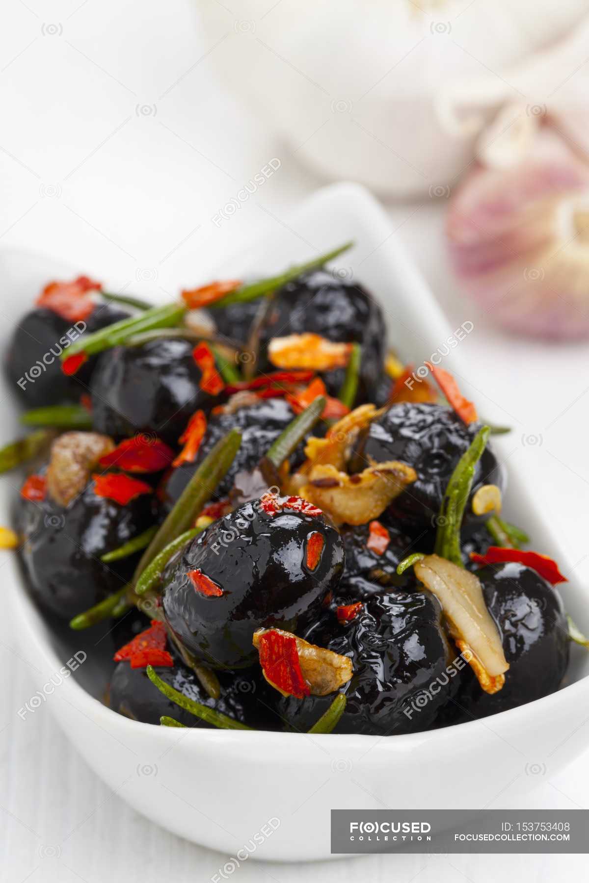 Marinated olives with rosemary, garlic and chilli on white plate