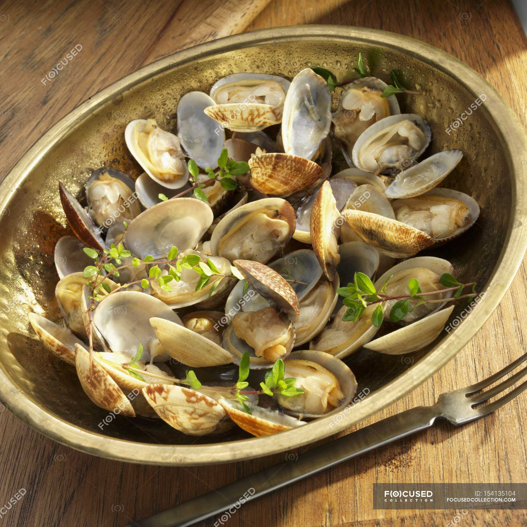 Closeup view of little neck clams with fresh herbs in copper bowl