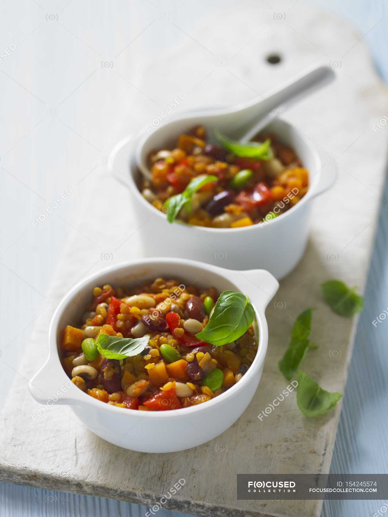 Bean stew with tomatoes and basil in white bowls on chopping board