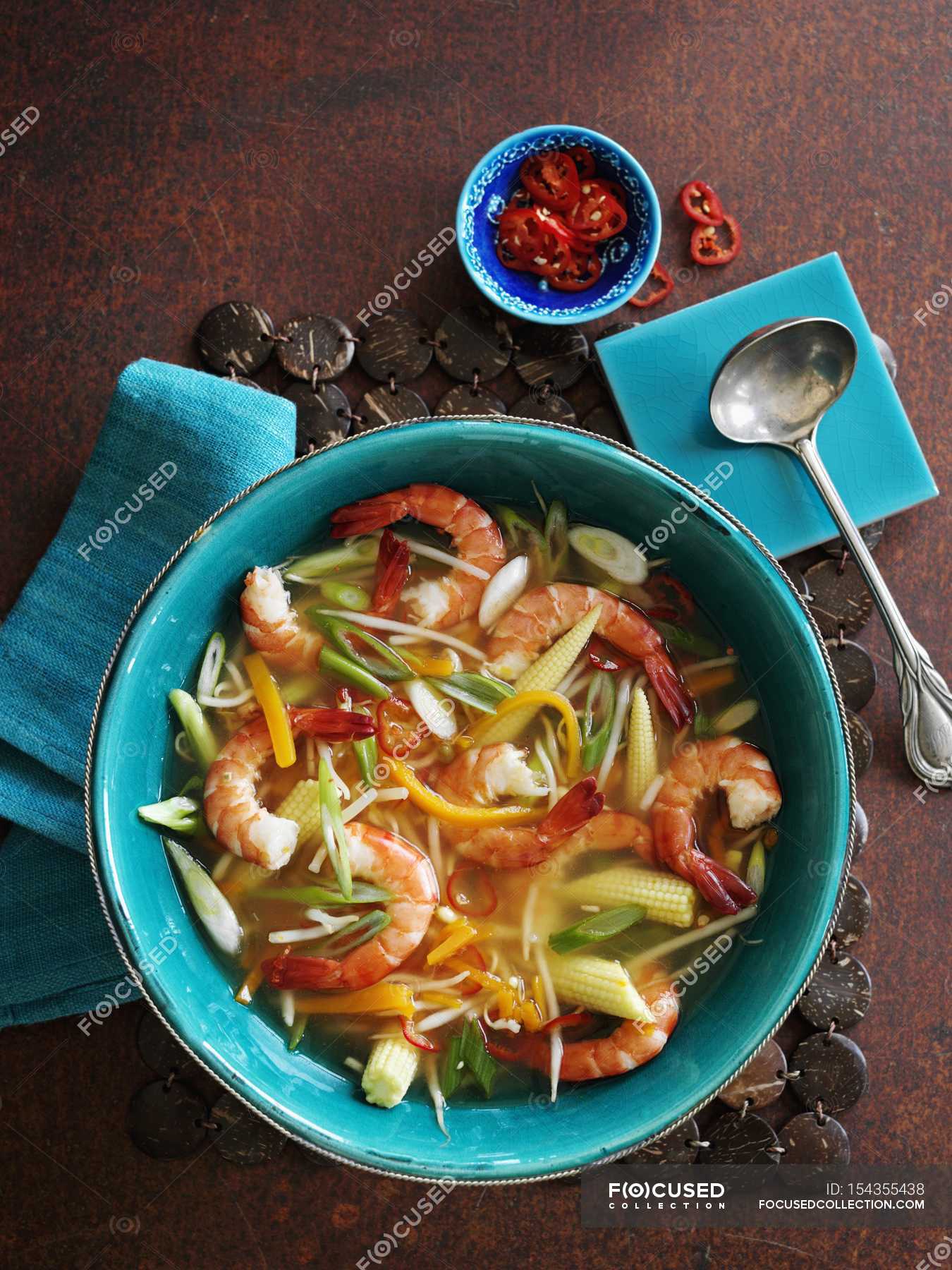 Spicy vegetable soup with prawns in green bowl over wooden surface ...