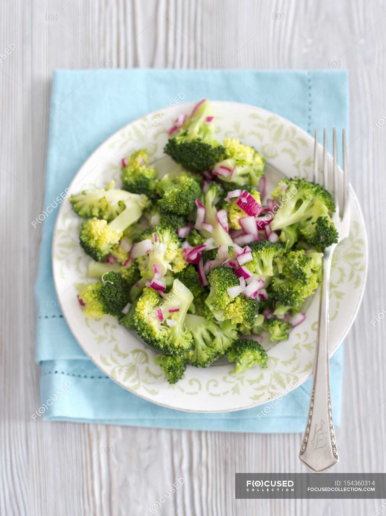 Steamed broccoli with red onion vinegar on white plate with fork over