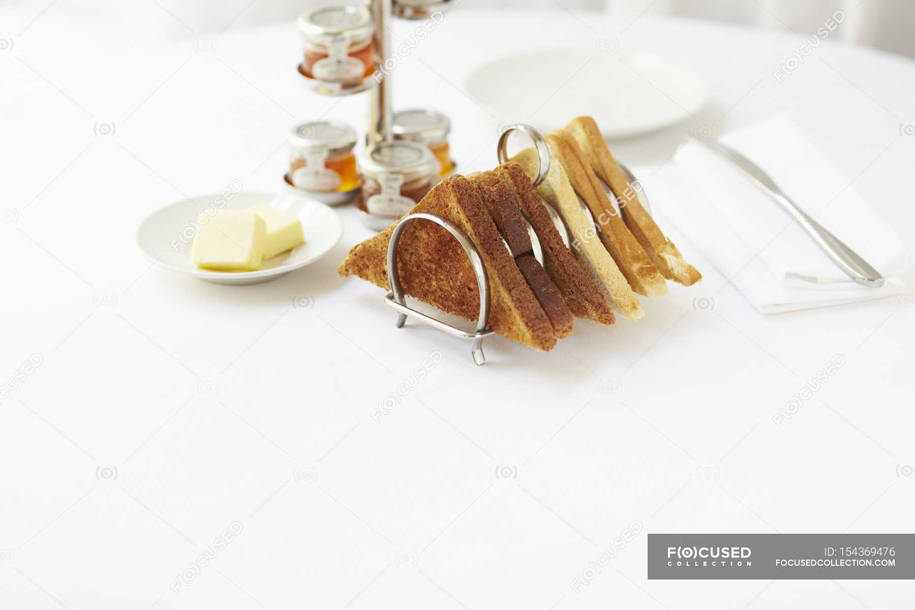 Elevated view of toasts in a toast rack served with butter and various jars of jam — white
