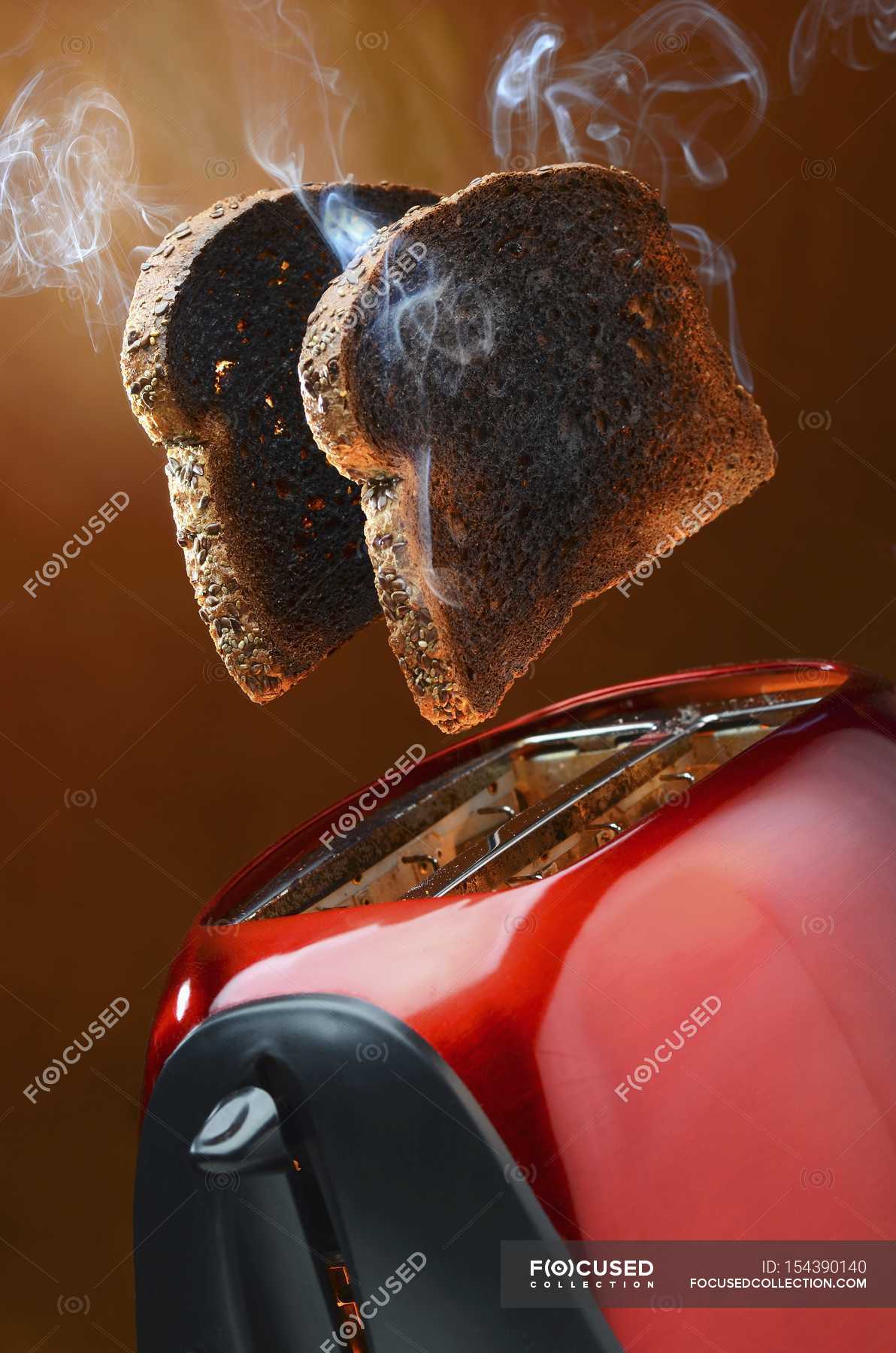 Closeup view of smoking wholemeal toast jumping out of a red toaster