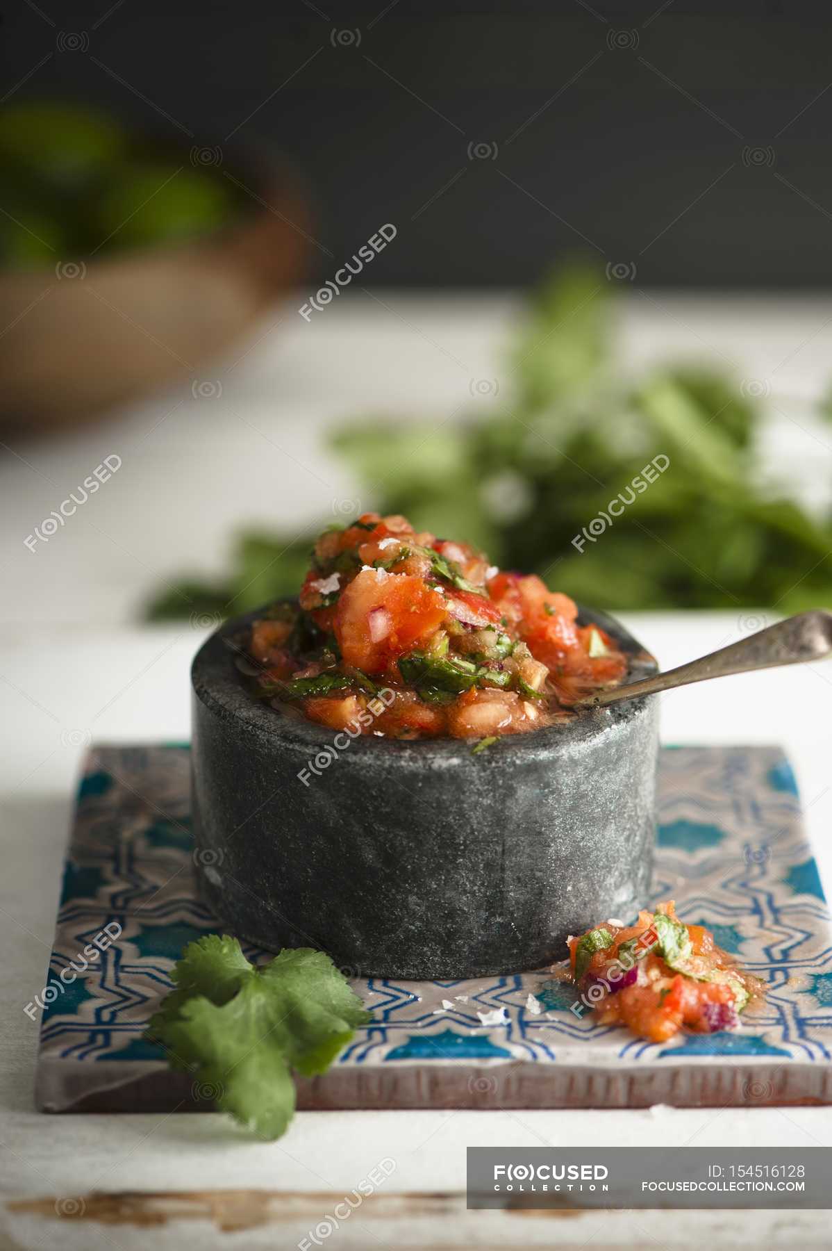 Tomato salsa with fresh coriander in stone pot over desk — taste, tasty