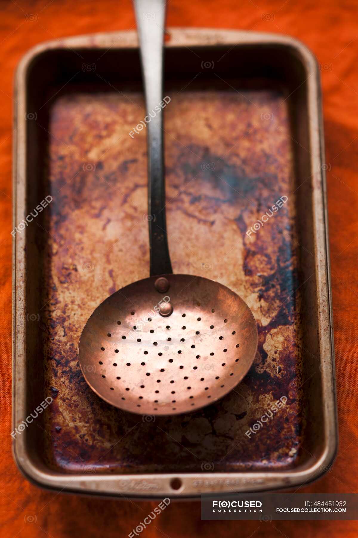 A burnt roasting tin with a strainer spoon — roasting pan, straining