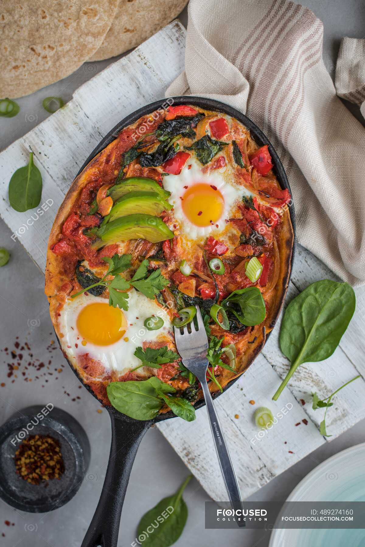 Huevos rancheros, mexican tortilla, tomato, pepper and chilli baked eggs wiyh avocado — spices