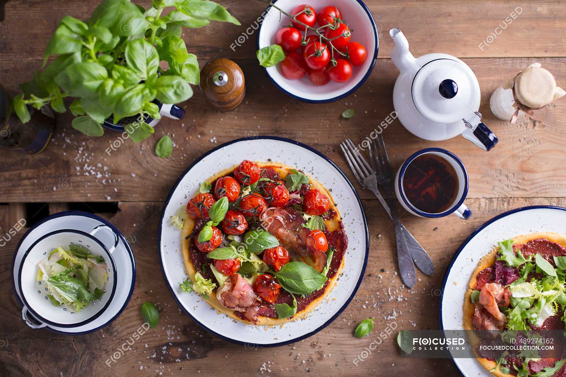 Gluten Free Pizza With Parma Ham, Fresh Basil Leaves And Cherry Tomatoes served on an enamel
