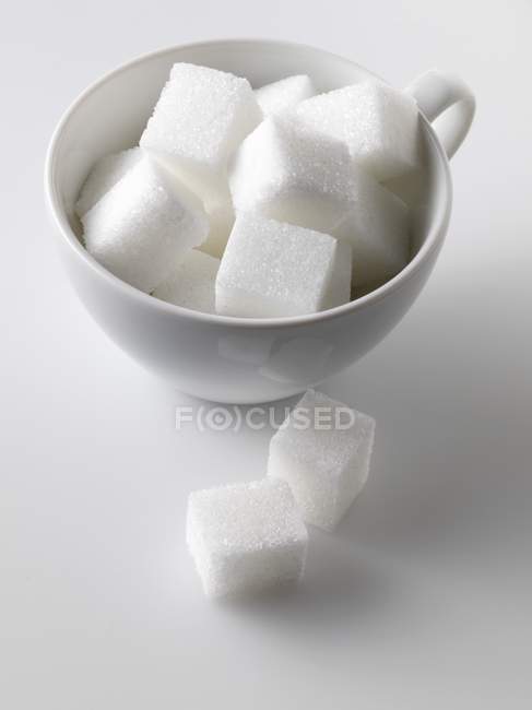 Vista de cerca de los cubos de azúcar en y al lado de la taza blanca - foto de stock