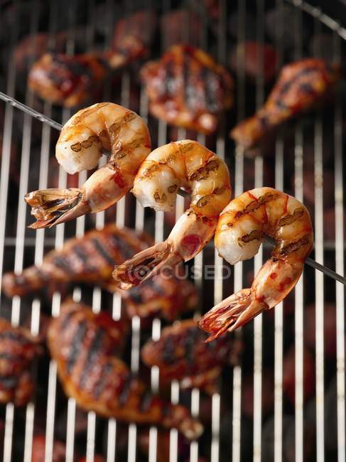 Closeup view of grilled, skewered shrimps over grill with chicken legs — Stock Photo