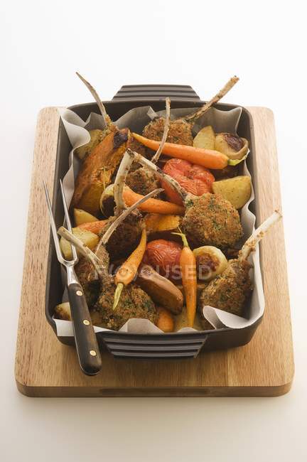 Elevated view of lamb chops with herbal crust and vegetables in baking pan on wooden board — Stock Photo