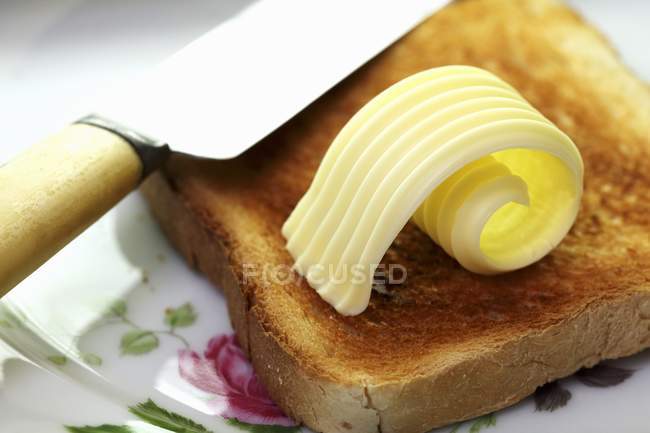Closeup view of a slice of toast with a curl of butter — Stock Photo