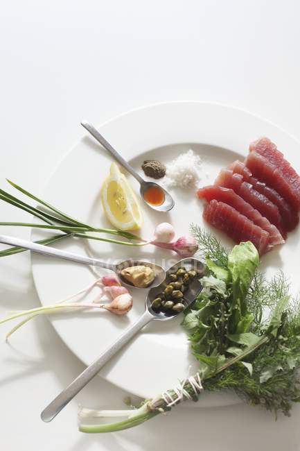 Roher Thunfisch, ein Bund Kräuter, Kapern und Frühlingszwiebeln in weißem Teller — Stockfoto