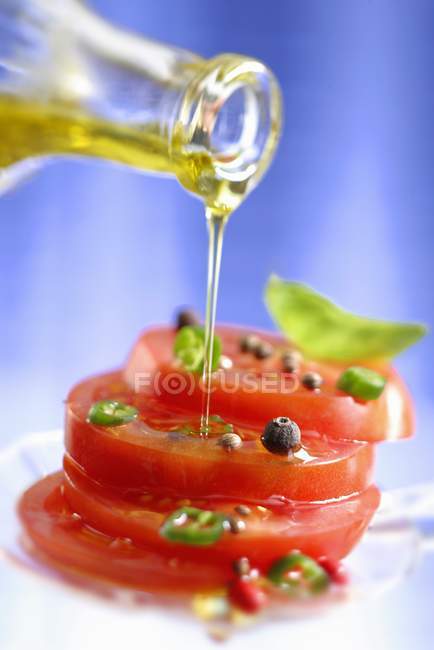 Tomates especiados rociados con aceite de oliva sobre fondo azul - foto de stock