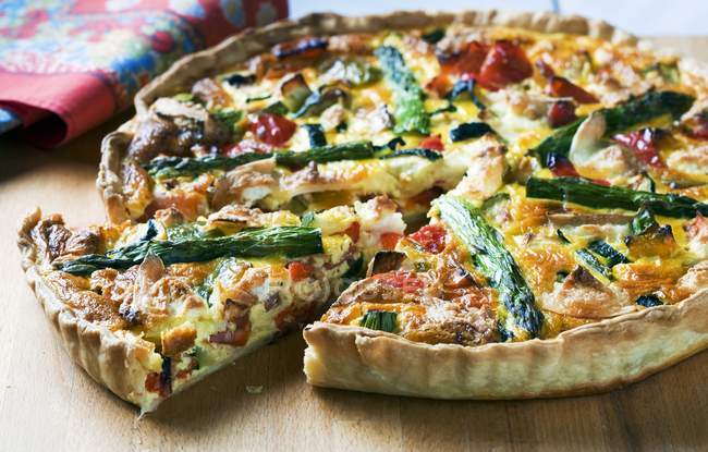 Provencal quiche partially sliced over wooden surface — Stock Photo