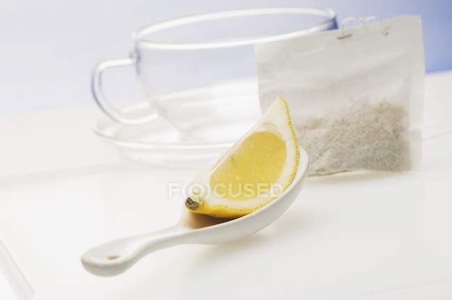Closeup view of a lemon wedge on a spoon, a tea bag and a tea cup — Stock Photo