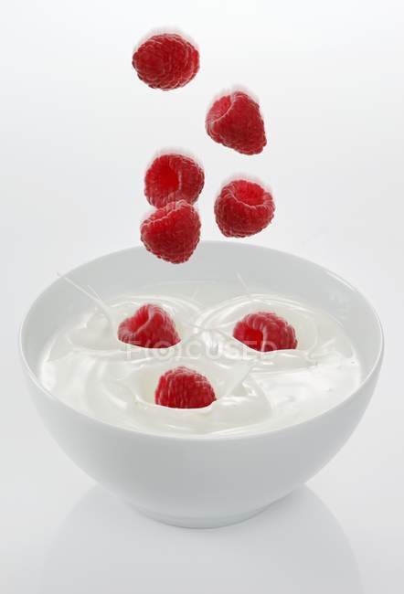 Raspberries falling in bowl with yogurt — Stock Photo