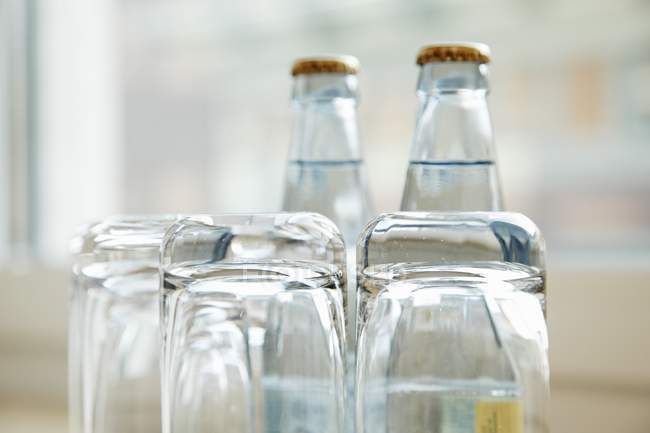 Vista de perto de copos de água de cabeça para baixo com garrafas de água no fundo — Fotografia de Stock