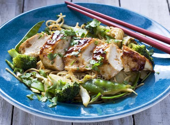 Chicken fillet with egg noodles, broccoli and mange tout on blue plate with wooden sticks — Stock Photo