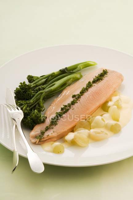 Trota veronique con salsa d'uva e broccoli su piatto bianco con forchetta e coltello — Foto stock