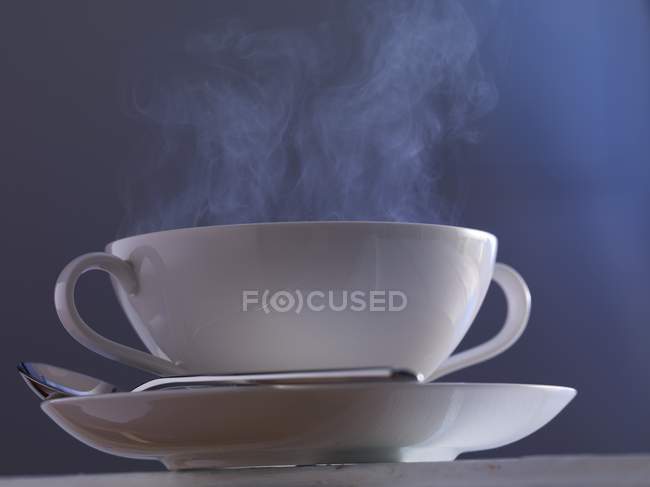 Vista close-up de uma xícara de sopa fumegante com colher na placa — Fotografia de Stock