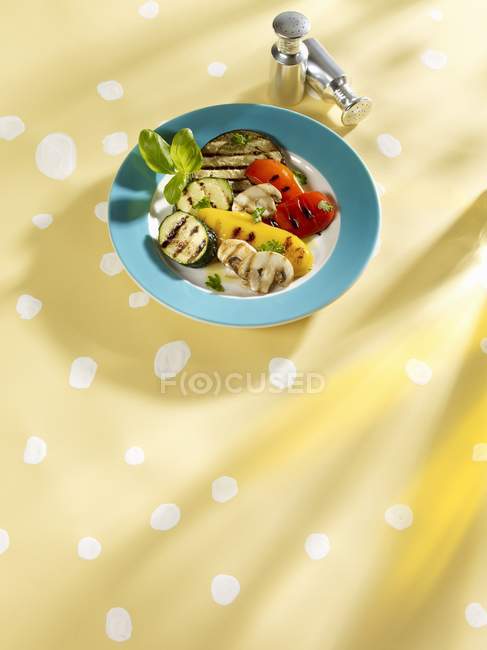 Légumes grillés sur plaque bleue sur surface jaune — Photo de stock