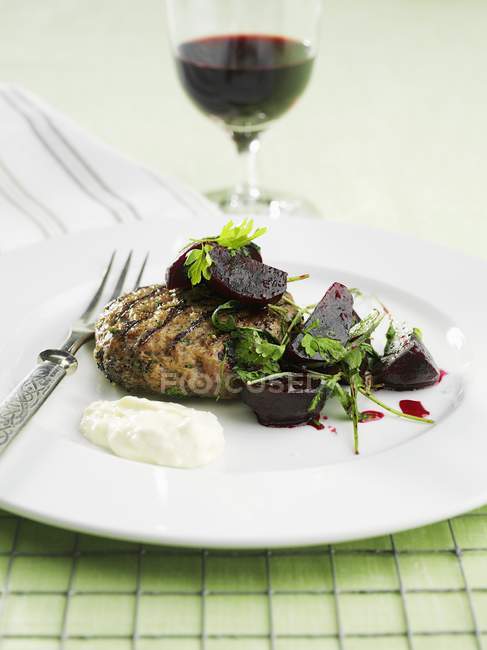 Hamburger con barbabietola su piatto bianco con forchetta e bicchiere di vino rosso su sfondo — Foto stock