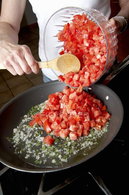 Frau fügt frische gewürfelte Tomaten in eine Pfanne auf dem Herd, Mittelteil — Stockfoto