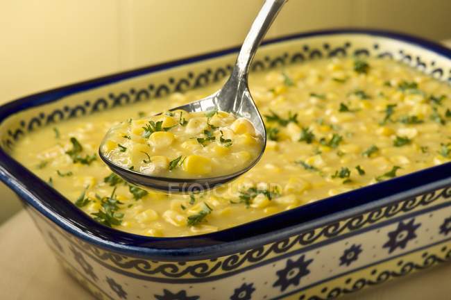 Cuchara antigua de maíz con crema; Maíz con crema en el plato para servir - foto de stock