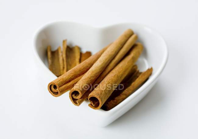 Closeup view of cinnamon sticks in a white heart-shaped bowl — Stock Photo
