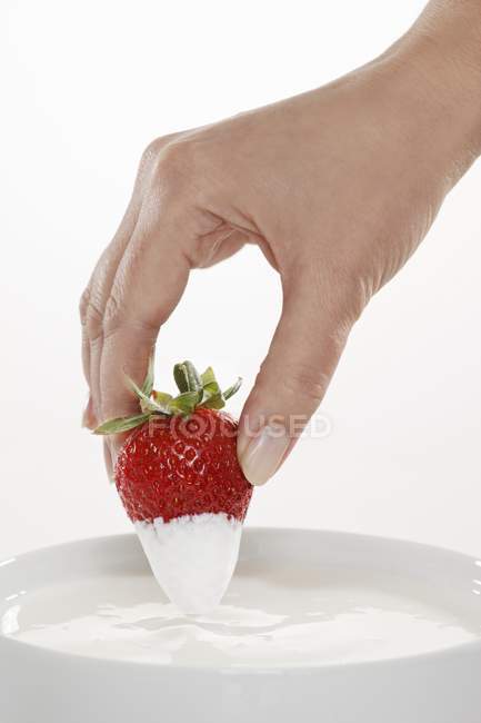 Hand dipping strawberry in yogurt — Stock Photo