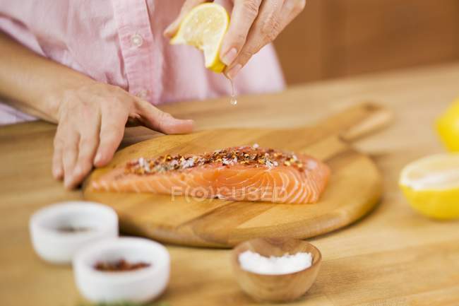 Femme pressant le jus de citron sur le saumon — Photo de stock