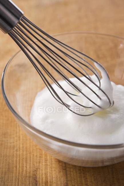 Closeup view of beaten egg white with whisk in glass bowl — Stock Photo