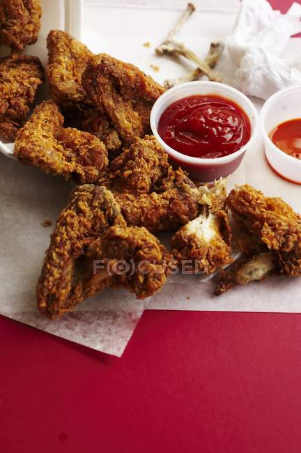 Vista elevada de las alas de pollo frito sobre papel con salsas de inmersión - foto de stock