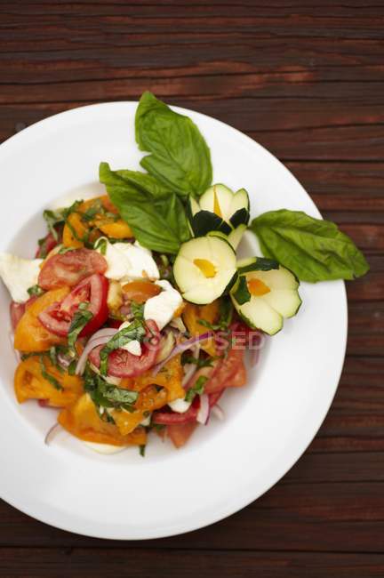 Салат из помидоров с моцареллой и базиликом на белой тарелке на деревянной поверхности — стоковое фото