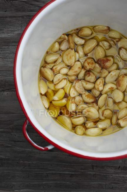 Roasted Garlic Cloves in Red Rimmed Pot  on wooden surface — Stock Photo