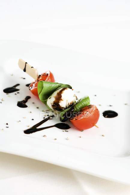 Pomodoro e mozzarella su bastoncino con aceto balsamico su piatto bianco — Foto stock
