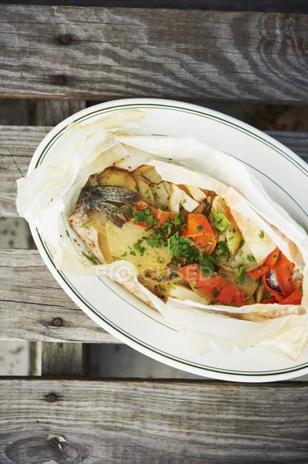 Trout en Papillote with Vegetables and Parsley on white plate over wooden surface — Stock Photo