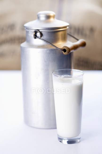 Glass of milk in front of a milk can — Stock Photo