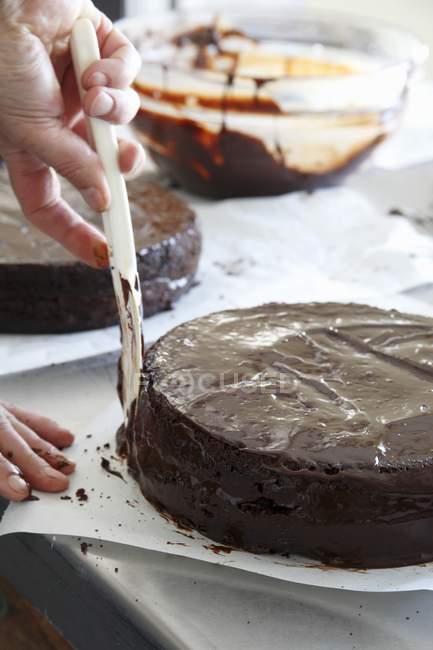 Nahaufnahme ausgeschnittene Ansicht von Person, die Schokoladenglasur mit Messer auf Kuchen verteilt — Stockfoto