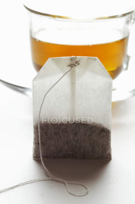Tea bag in front of a cup — Stock Photo