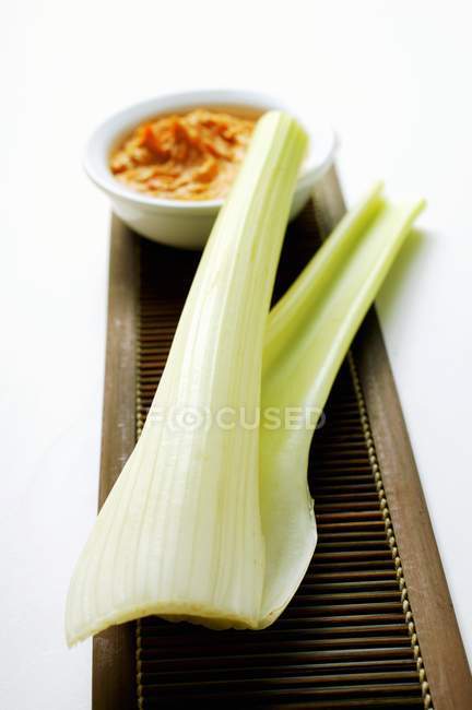 Celery and dip on wooden desk over white background — Stock Photo