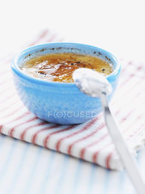 Closeup view of Creme brulee in blue bowl with spoon — Stock Photo