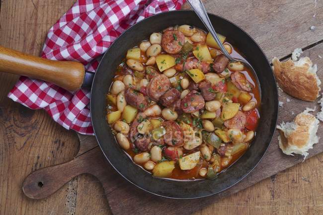 Rustic bean and sausage stew in frying pan over wooden desk — Stock Photo