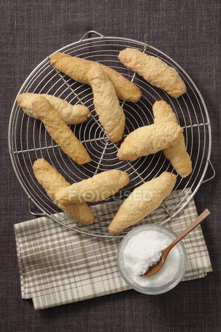 Top view of Zezettes de Sete French pastries on cooling wire rack with icing sugar in jar — Stock Photo
