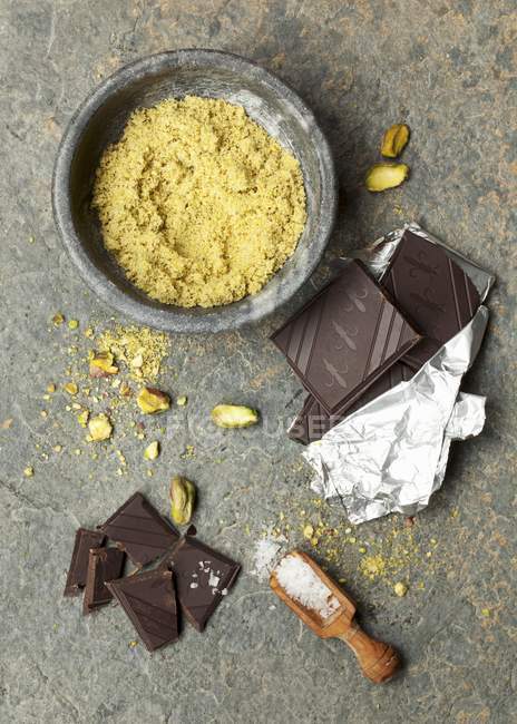 Top view of whole and powdered pistachio nuts with chocolate bars and salt — Stock Photo