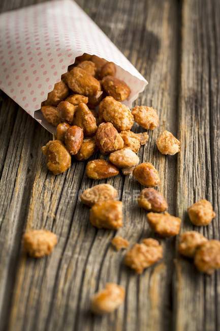 Closeup view of homemade roasted almonds with paper bag on wooden surface — Stock Photo